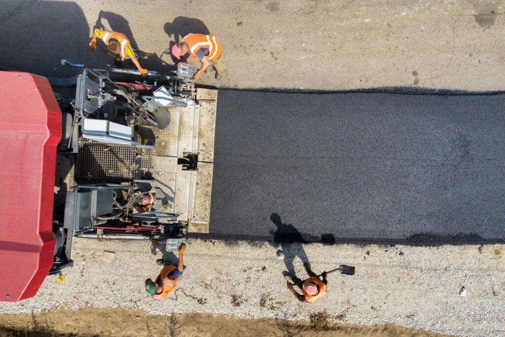 Aerial view of four construction workers paving a road with asphalt using heavy machinery, showcasing expert asphalt resurfacing in New Hampshire.