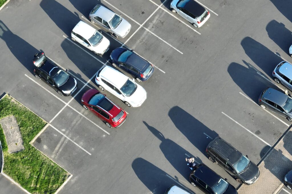 Aerial view of cars parked in a lot with fresh sealcoating and striping in New Hampshire; some spaces are empty, and one person is walking near the parked vehicles.