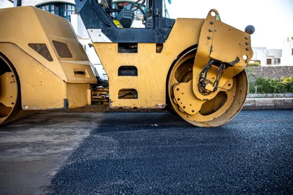 A yellow road roller compacts freshly laid asphalt on a street, leveling the surface.