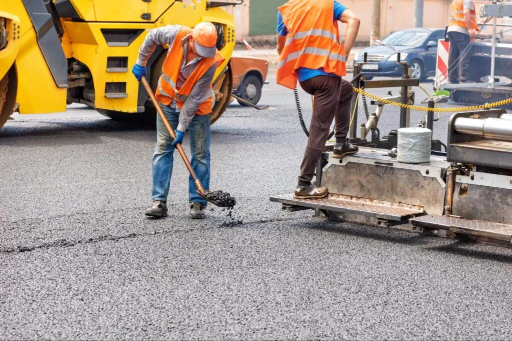 Construction workers in orange vests and helmets skillfully provide asphalt services, paving a road with machinery and shovels. Construction workers in orange vests and helmets skillfully provide asphalt services, paving a road with machinery and shovels.